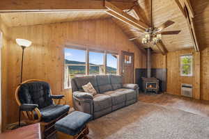 Living room with wooden walls, a wood stove, wooden ceiling, carpet, and ceiling fan