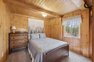 Carpeted bedroom with wood walls and a wood ceiling with exposed beams