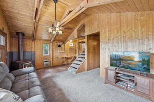Living area with wooden ceiling, a wood stove, stairway, wooden walls, and carpet