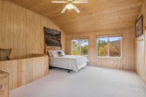 Bedroom with wooden walls, vaulted ceiling, carpet floors, wooden ceiling, and a ceiling fan