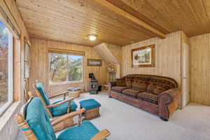 Living area with a wood stove, a wood ceiling with exposed beams, wood walls, and carpet flooring