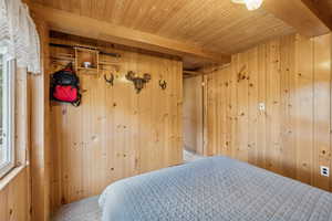 Bedroom featuring wood walls, carpet flooring, a wooden ceiling with exposed beams, a closet, and multiple windows