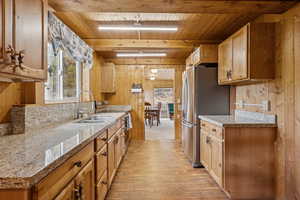 Kitchen with wood walls, freestanding refrigerator, white stove, light wood-style floors, and a wood ceiling with exposed beams