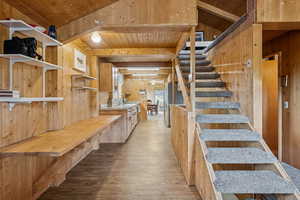 Stairs featuring wood finished floors, wood walls, and a wooden ceiling with exposed beams