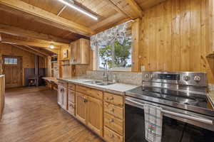 Kitchen with stainless steel electric range oven, wood walls, light stone countertops, a wood stove, and dark wood-style floors