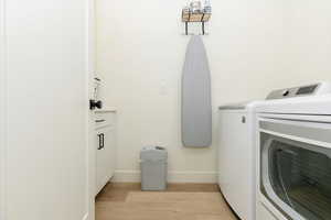 Washroom with light wood-type flooring, separate washer and dryer, and cabinet space