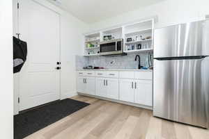 Kitchen with appliances with stainless steel finishes, white cabinets, light wood-style floors, open shelves, and tasteful backsplash