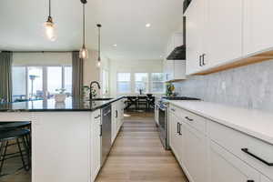 Kitchen with white cabinetry, stainless steel appliances, decorative light fixtures, a kitchen breakfast bar, and decorative backsplash