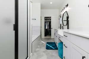Full bathroom featuring double vanity, a walk in closet, a garden tub, a shower stall, and recessed lighting