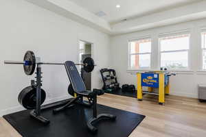 Workout area with healthy amount of natural light, light wood finished floors, recessed lighting, and a tray ceiling