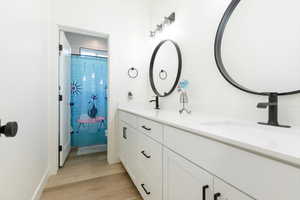 Bathroom with double vanity, light wood-style floors, and a shower with shower curtain