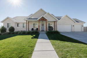 View of front of house featuring a porch, stone siding, a front lawn, a garage, and concrete driveway