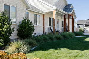View of side of home featuring stone siding, a shingled roof, a lawn, and covered porch