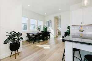 Kitchen with white cabinetry, dark stone counters, a kitchen bar, light wood-style floors, and recessed lighting