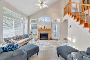 Carpeted living room with high vaulted ceiling, a glass covered fireplace, plenty of natural light, a ceiling fan, and stairway