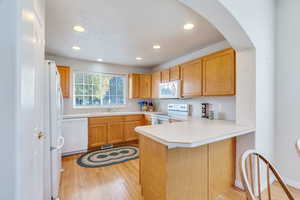 Kitchen featuring light countertops, a peninsula, light wood-style floors, white appliances, and recessed lighting
