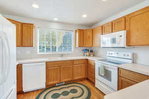 Kitchen featuring white appliances, light wood-type flooring, light countertops, recessed lighting, and brown cabinets