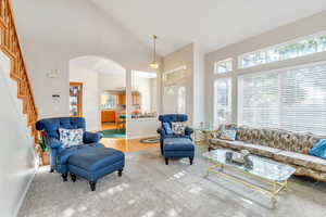 Living room with high vaulted ceiling, arched walkways, wood finished floors, and stairs