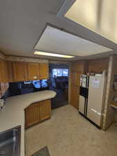 Kitchen featuring freestanding refrigerator, light countertops, a peninsula, and brown cabinets