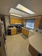 Kitchen featuring brown cabinetry, wallpapered walls, stainless steel appliances, light countertops, and under cabinet range hood