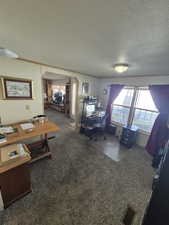 Office area featuring dark carpet, arched walkways, a textured ceiling, and crown molding