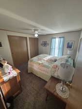 Carpeted bedroom with two closets, a textured ceiling, ceiling fan, and ornamental molding