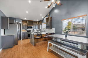 Kitchen featuring high vaulted ceiling, light stone counters, a peninsula, gray cabinetry, and appliances with stainless steel finishes