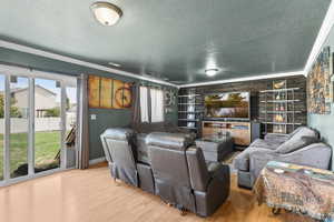 Cinema with crown molding, wood finished floors, healthy amount of natural light, a textured ceiling, and wooden walls