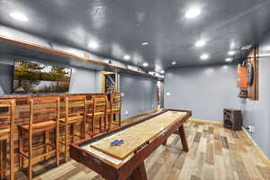 Playroom featuring a textured ceiling, light wood finished floors, recessed lighting, and bar area