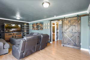 Living area featuring a textured ceiling, wood finished floors, ornamental molding, and a barn door