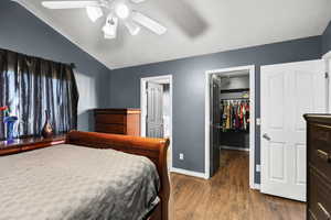 Bedroom featuring a walk in closet, dark wood-style floors, vaulted ceiling, ceiling fan, and a textured ceiling