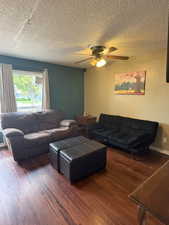 Living room featuring dark wood finished floors, ceiling fan, and a textured ceiling