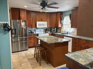 Kitchen with white appliances, a breakfast bar area, brown cabinets, a kitchen island, and a ceiling fan
