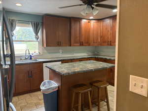 Kitchen featuring a textured wall, brown cabinetry, a kitchen bar, freestanding refrigerator, and recessed lighting