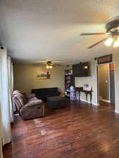Living area with ceiling fan, a textured ceiling, and dark wood-style floors