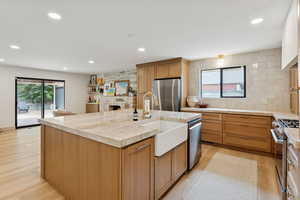 Kitchen featuring an island with sink, recessed lighting, stainless steel appliances, light wood-style flooring, and a fireplace