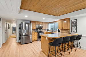 Kitchen featuring wooden ceiling, a kitchen breakfast bar, light countertops, appliances with stainless steel finishes, and recessed lighting