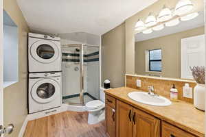 Full bathroom with a stall shower, vanity, light wood-type flooring, estacked washer and dryer, and a textured ceiling