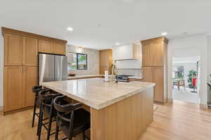 Kitchen featuring a breakfast bar area, light wood-type flooring, a center island with sink, recessed lighting, and backsplash