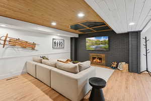 Home theater with recessed lighting, wooden ceiling, brick wall, light wood finished floors, and a brick fireplace