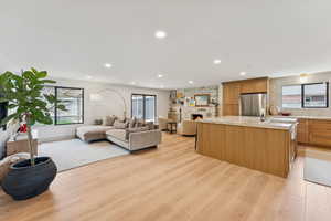 Kitchen with open floor plan, an island with sink, freestanding refrigerator, light wood-style flooring, and a large fireplace
