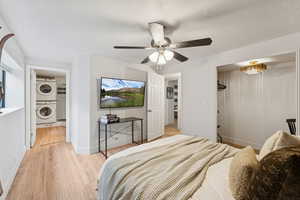 Bedroom with light wood finished floors, stacked washer / drying machine, a closet, ceiling fan, and connected bathroom