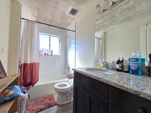 Bathroom with shower / bathtub combination with curtain, a textured ceiling, vanity, and light wood finished floors