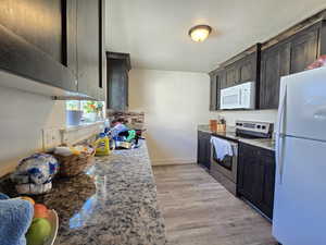 Kitchen featuring white appliances, light stone countertops, light wood-style floors, and a textured ceiling