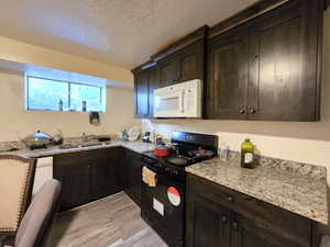Kitchen with white appliances, dark brown cabinets, a textured ceiling, light wood-type flooring, and light stone countertops
