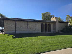 Rear view of house featuring brick siding, a lawn, a chimney, and a patio