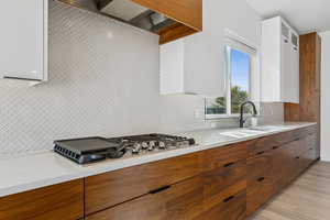Kitchen with brown cabinets, decorative backsplash, custom exhaust hood, and modern cabinets