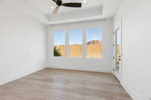 Spare room with a tray ceiling, light wood-style floors, and ceiling fan