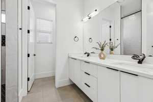 Bathroom with double vanity, a tile shower, and light tile patterned floors