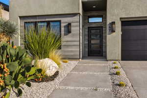 Entrance to property featuring stucco siding, stone siding, and a garage